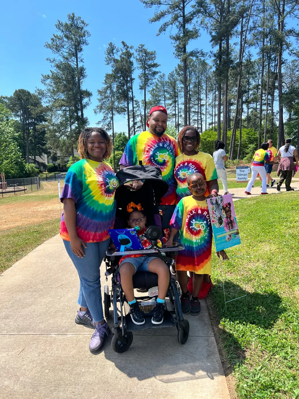 Cupcake in her wheelchair with her family in matching tie-dye shirts at a Walk & Roll event